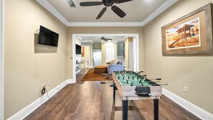 A room with a foosball table, a ceiling fan, and a television mounted on the wall. - Walking on Sunshine: Golf Cart & Movie Theater! 2 Pools! CLOSE To The Beach! (Destin)