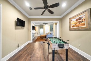 A room with a foosball table, a ceiling fan, and a television mounted on the wall. - Walking on Sunshine: Golf Cart & Movie Theater! 2 Pools! CLOSE To The Beach! (Destin)