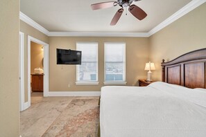 Un dormitorio con cama, ventilador de techo, televisión y ventana con persianas.