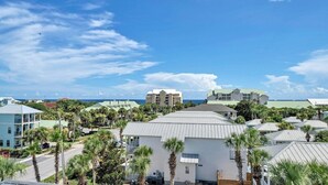 A coastal hotel with multiple buildings, palm trees, and a clear view of the ocean. - Walking on Sunshine: Golf Cart & Movie Theater! 2 Pools! CLOSE To The Beach! (Destin)