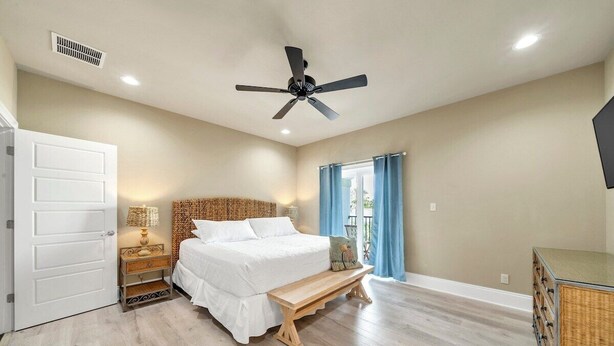 A bedroom with a bed, a ceiling fan, a window with curtains, a bedside table, and a nightstand. - Walking on Sunshine: Golf Cart & Movie Theater! 2 Pools! CLOSE To The Beach! (Destin)