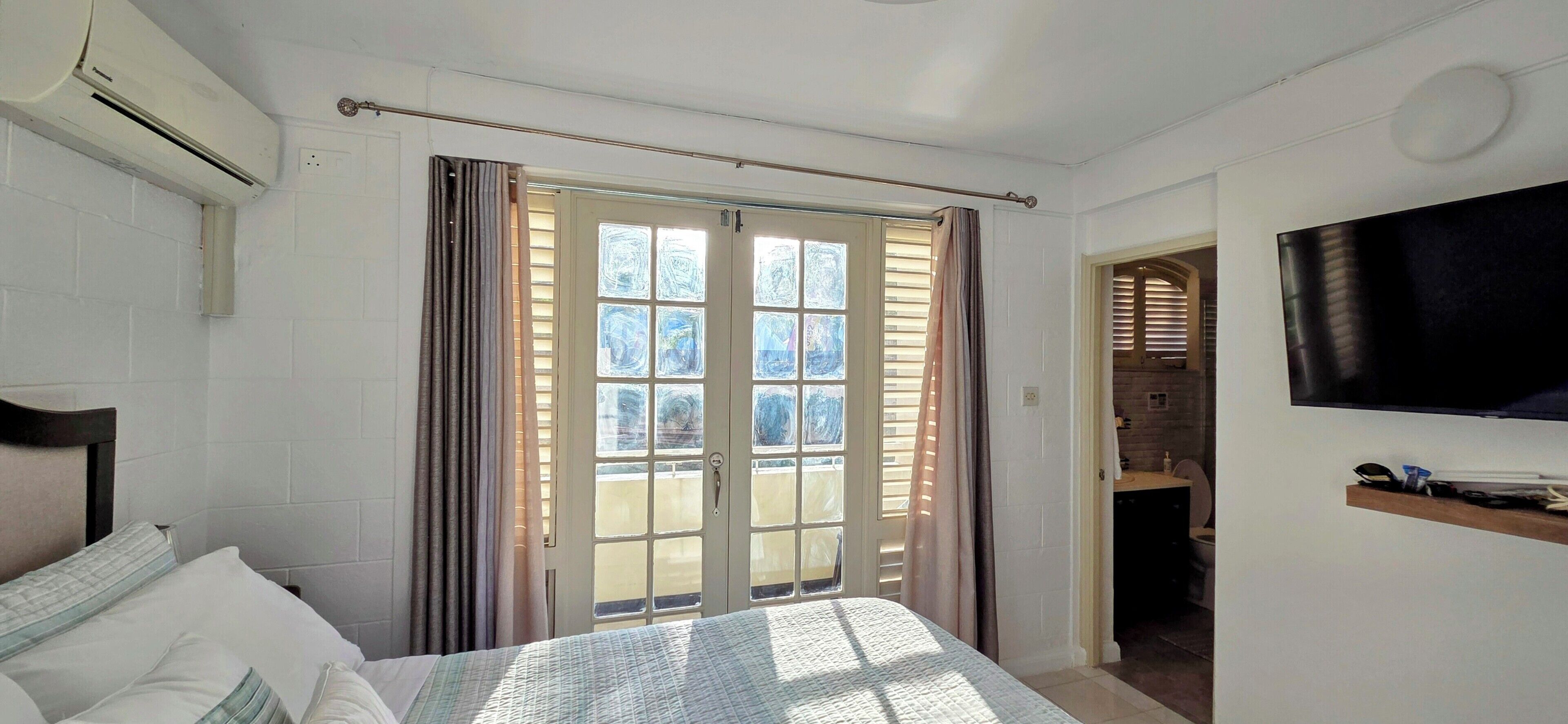 A bedroom with a bed, a TV mounted on the wall, and a sliding glass door leading to a balcony.