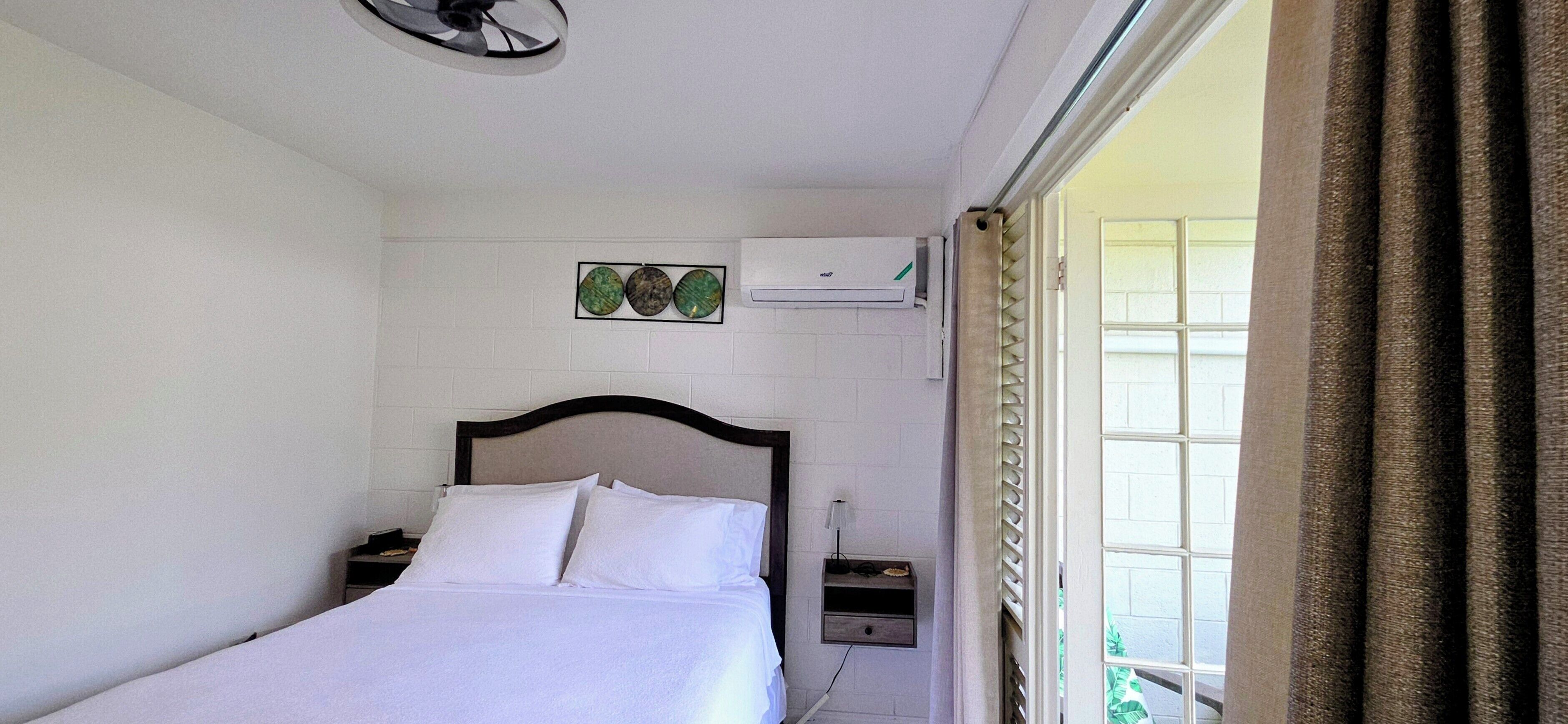 Ein Hotelzimmer mit einem Bett, einem Nachttisch, einer Wand-Klimaanlage und einem Fenster mit Vorhängen.
