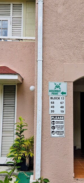 A building exterior with a sign indicating an assembly point and a list of room numbers. - Ocho Rios Beach Condo-Pool + 3-Min Walk to Beach (Ocho Rios)