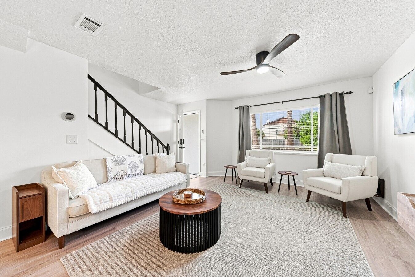 Un salon moderne comprenant un canapé, deux fauteuils, une table basse et un ventilateur de plafond.