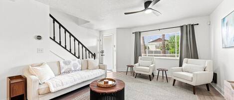 A modern living room with a sofa, two armchairs, a coffee table, and a ceiling fan.
