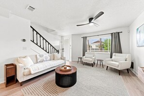 A modern living room with a sofa, two armchairs, a coffee table, and a ceiling fan.