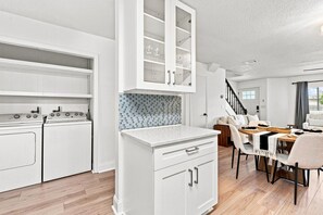 A modern kitchen with white cabinetry, a tiled backsplash, and a dining area with a wooden table and chairs.