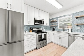 A modern kitchen with stainless steel appliances, white cabinetry, and a tiled backsplash.