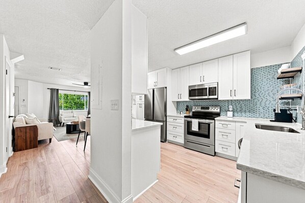 A modern kitchen with white cabinets, stainless steel appliances, and a tiled backsplash.