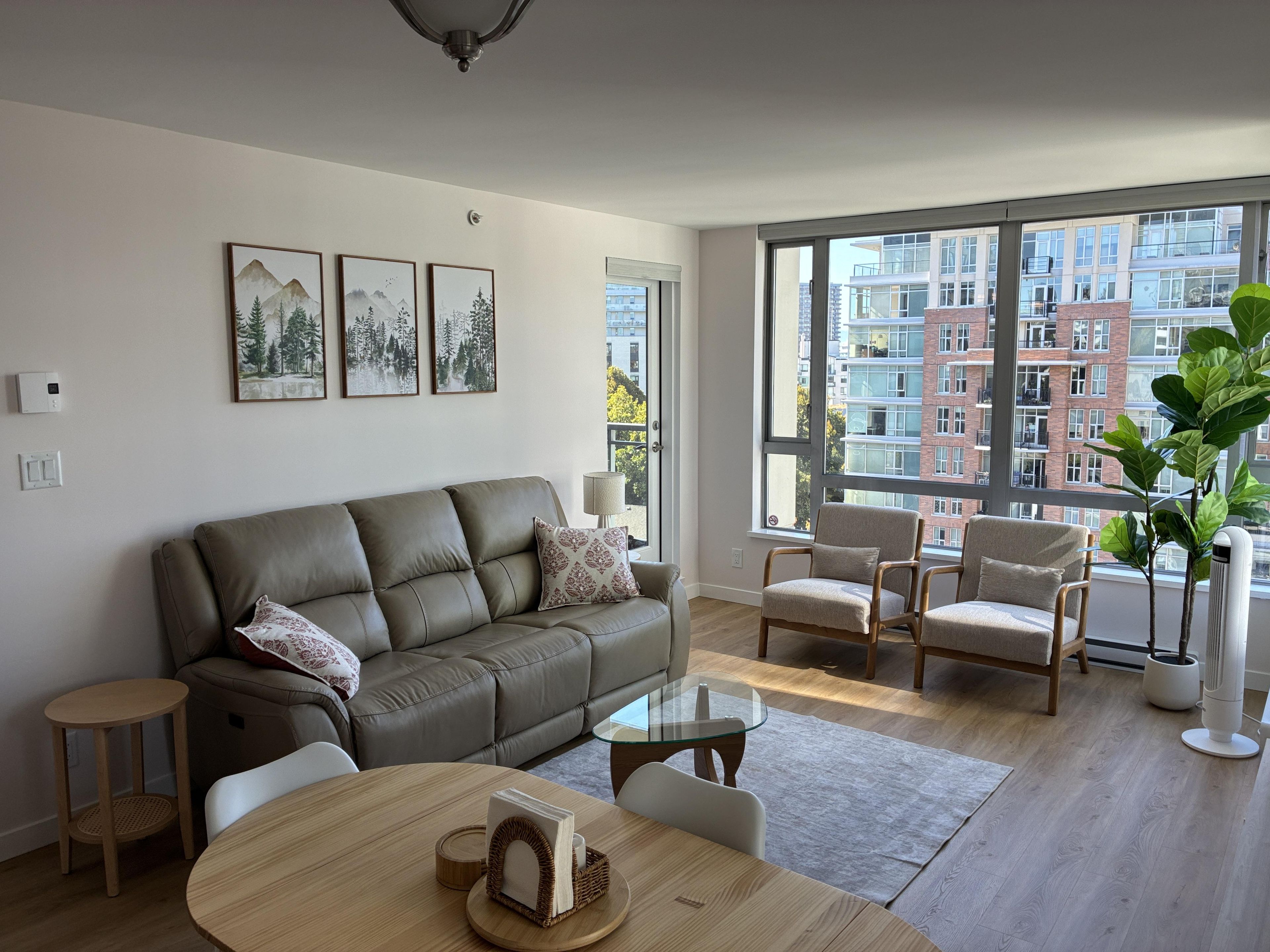 Un salon moderne avec un canapé en cuir, une table basse en verre et une vue sur le paysage urbain grâce à de grandes fenêtres.