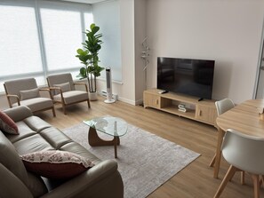 Een moderne woonkamer met een bank, stoelen, een glazen salontafel, een televisie en een eettafel.