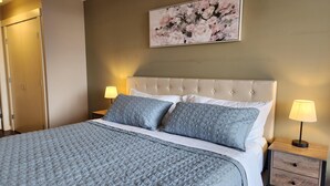 Uma cama bem arrumada com cobertura acolchoada, cabeceira estofada e duas luminárias de cabeceira.