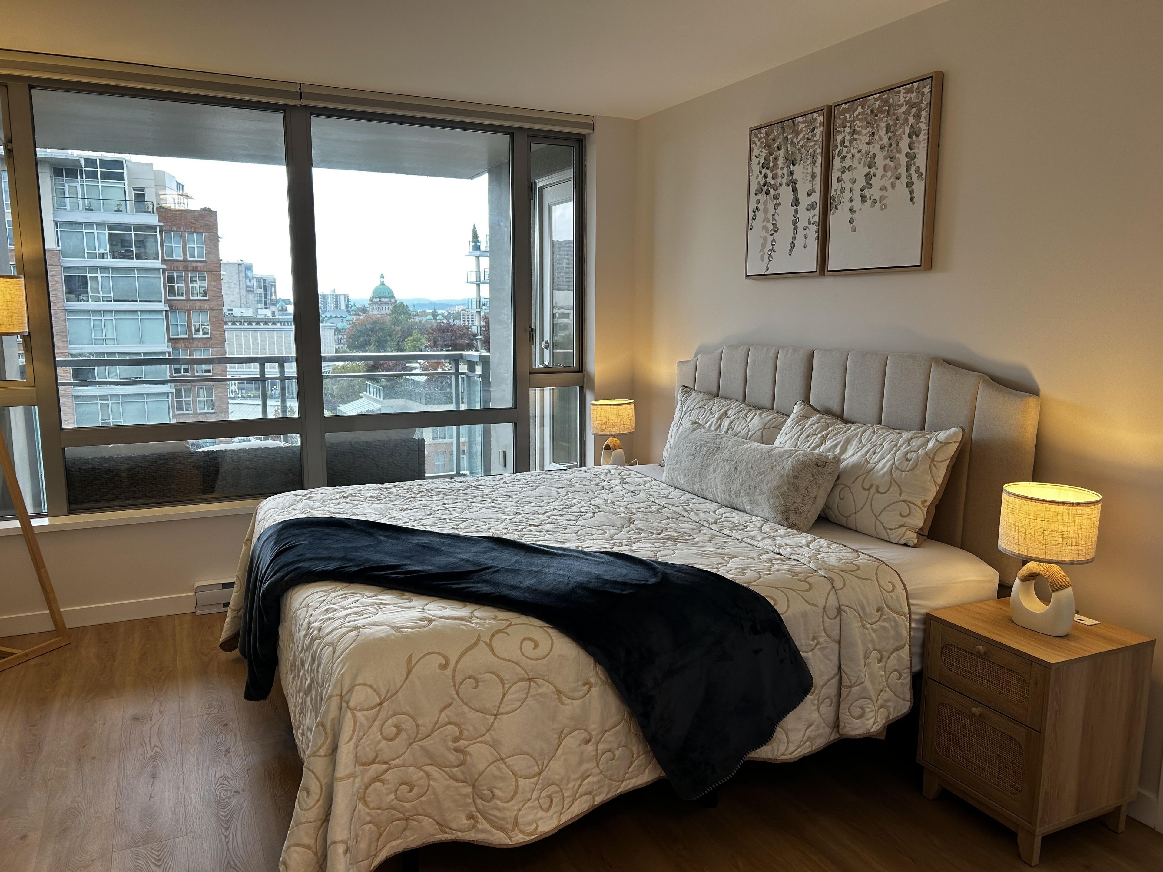 Une chambre à coucher avec une grande fenêtre, un lit avec une tête de lit, des lampes de chevet et une table de chevet.