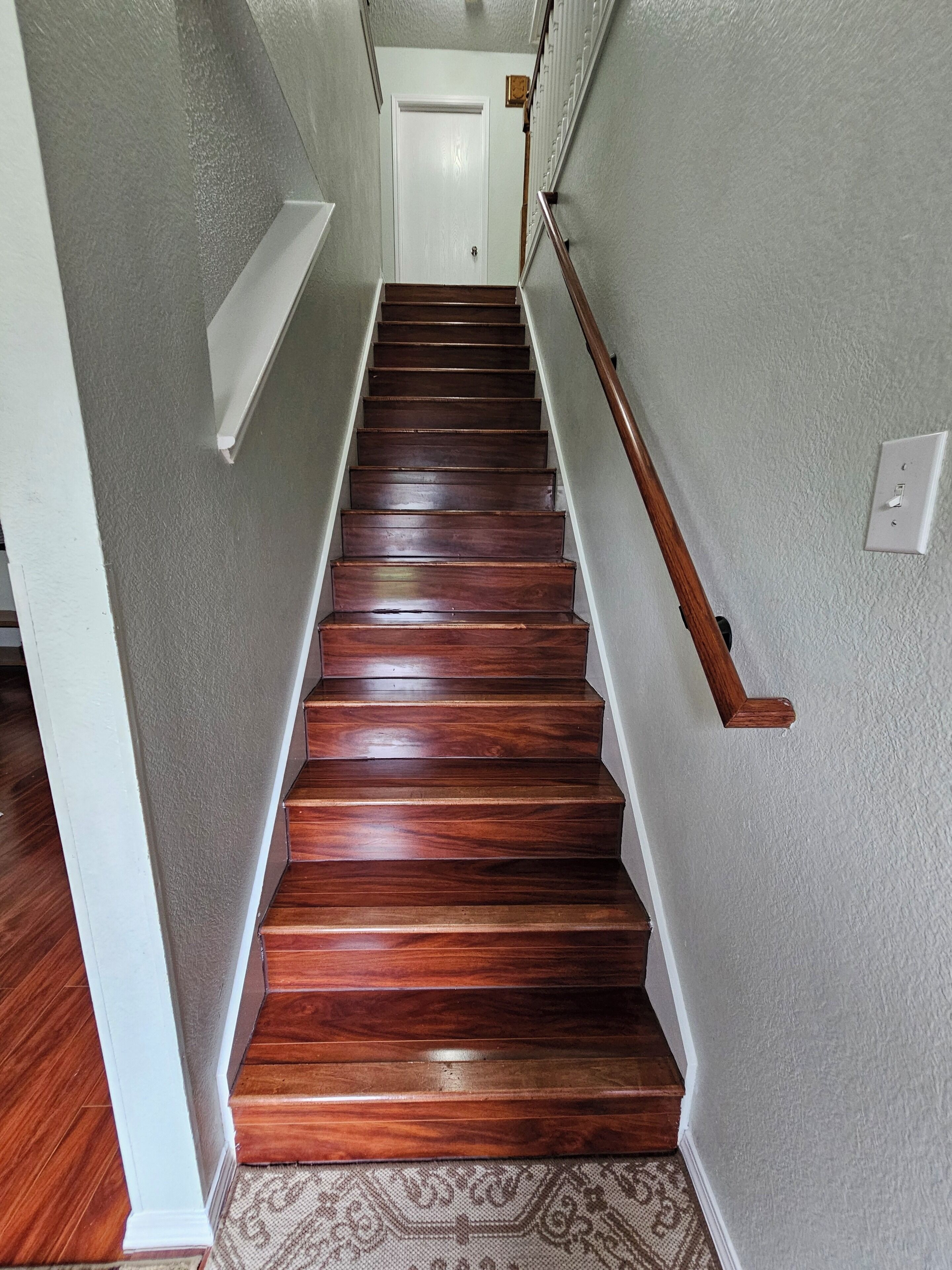 Una escalera de madera con barandilla que lleva a una puerta blanca en la parte superior.