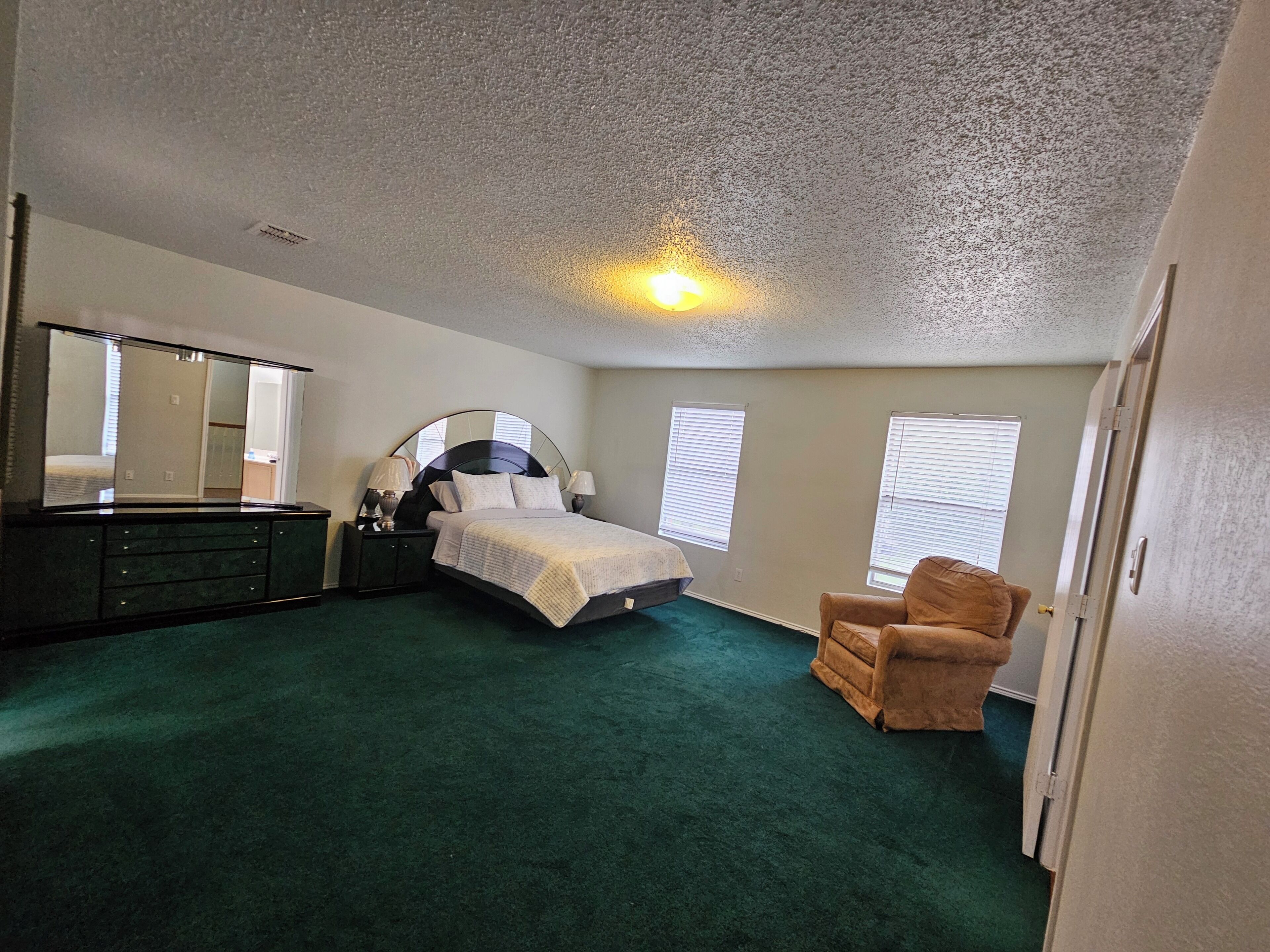 A bedroom with a bed, dresser, chair, and a large mirror.