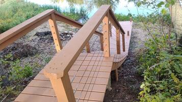 Un puente de madera con baranda metálica que conduce a una plataforma de madera sobre un cuerpo de agua.