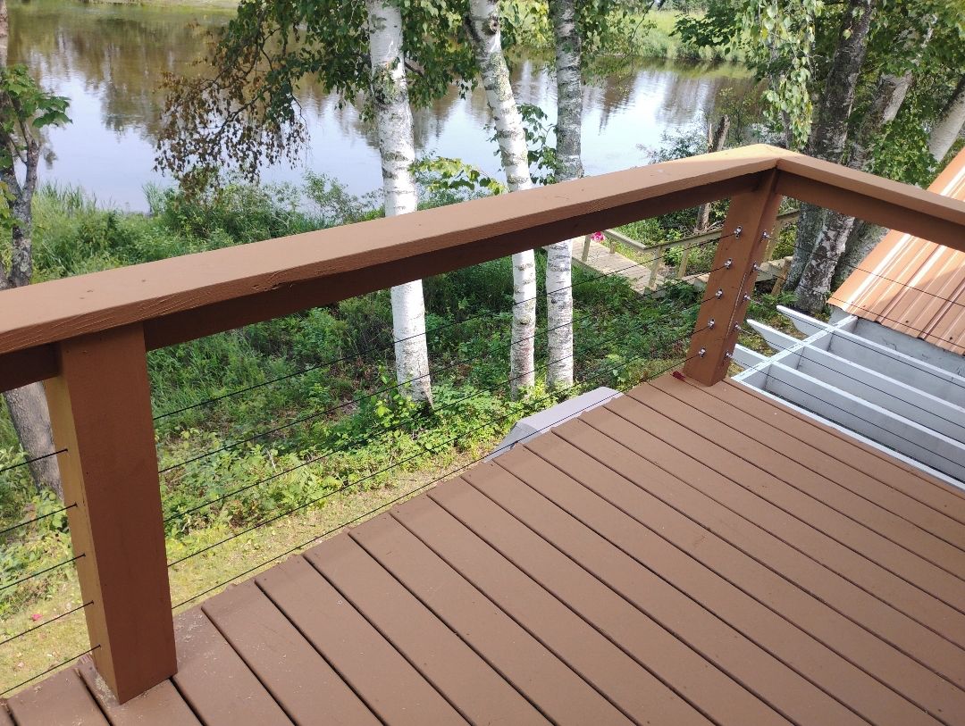 A wooden deck with a metal railing overlooking a body of water and greenery.