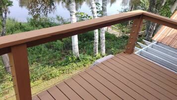 A wooden deck with a metal railing overlooking a body of water and greenery.