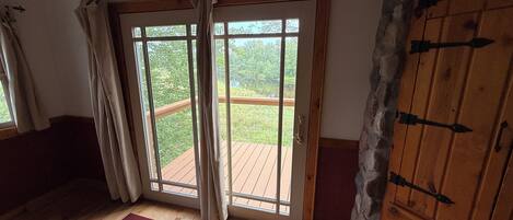 A room with a wooden floor, a red and white rug, a sliding glass door leading to an outdoor deck, and a stone wall.