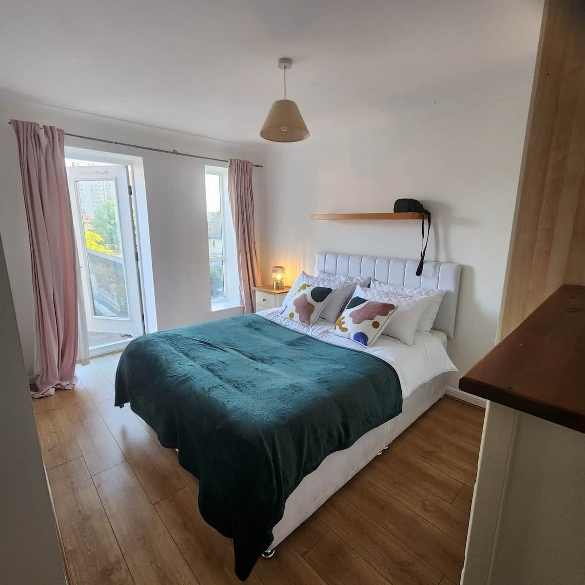 A bedroom with a bed, a bedside table, a lamp, and a window with curtains.