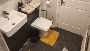 A bathroom with a white sink, toilet, and a mirror above the sink. There are towels and toiletries on the counter. - Modern Bright Riverside Stay (London)