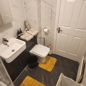 Ein Badezimmer mit einem weißen Waschbecken, einer Toilette und einem Spiegel über dem Waschbecken. Auf der Ablage liegen Handtücher und Pflegeprodukte.
