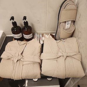 A bathroom with a bathtub, two bottles of hand soap, a pair of slippers, and two towels. - Modern Bright Riverside Stay (London)