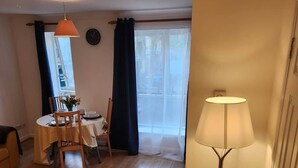 A room with a dining table set for two, a lamp, and a view through a window with curtains. - Modern Bright Riverside Stay (London)
