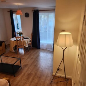 Ein Zimmer mit Esstisch für zwei Personen, einer Lampe und Blick durch ein mit Vorhängen drapiertes Fenster.