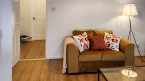 A living room with a sofa, a lamp, and a ceiling light fixture. - Modern Bright Riverside Stay (London)