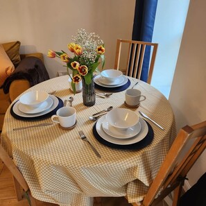 A round dining table with a checkered tablecloth, white plates, bowls, cups, cutlery, and a vase with flowers. - Modern Bright Riverside Stay (London)
