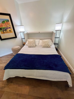 Un letto ben rifatto con copripiumino a righe e due cuscini, una lampada da comodino e un quadro appeso al muro.