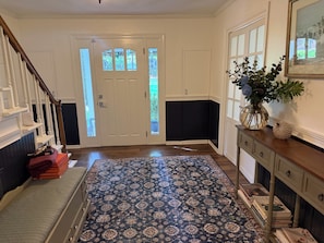 A hallway with a patterned rug, a staircase, a door with glass panels, and a vase with flowers on a console table. - 5BR Private Aiken Home on 2 Acres - 30 Min to Augusta National - Masters Week (Aiken)