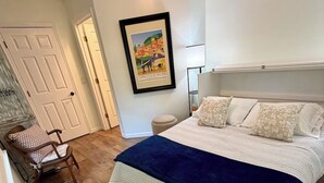Un dormitori amb un llit, una cadira, un quadre a la paret i una porta.