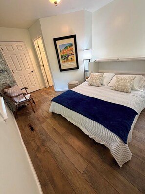 Ein Schlafzimmer mit einem Bett, einem Sessel, einem gerahmten Bild an der Wand und einer Tür.