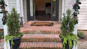 Entrada d'una casa amb un porxo, un estri de benvinguda i dues plantes en testos.