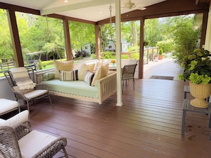 A covered outdoor seating area with wicker furniture, a cushioned bench, and a potted plant. - 5BR Private Aiken Home on 2 Acres - 30 Min to Augusta National - Masters Week (Aiken)