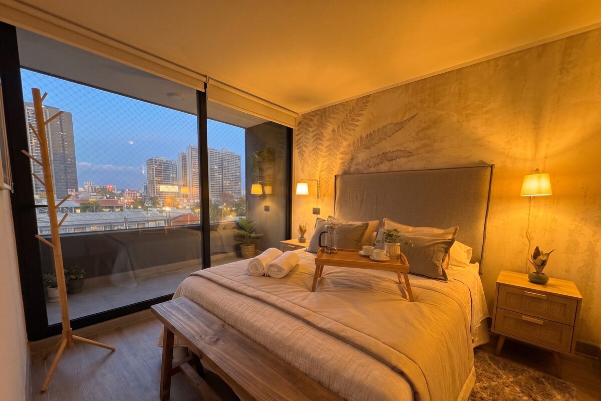 A modern bedroom with a large bed, bedside lamps, a tray with cups and a pitcher, and a city view through a large window.