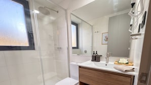A modern bathroom with a glass shower enclosure, a toilet, a sink with a mirror, and a wooden vanity. - Santiago Metro Ecuador - Domus Travels (Santiago)