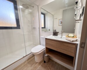 A modern bathroom with a glass shower enclosure, a toilet, a sink with a mirror, and a wooden vanity. - Santiago Metro Ecuador - Domus Travels (Santiago)