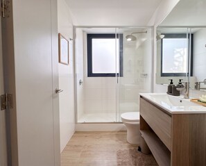 A modern bathroom with a glass shower enclosure, a toilet, and a vanity with a mirror. - Edificio O2 Santiago by Domus Travels (Santiago)