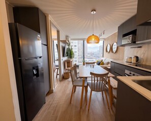 A modern kitchen with a built-in refrigerator, wooden dining table, and a city view. - Edificio O2 Santiago by Domus Travels (Santiago)