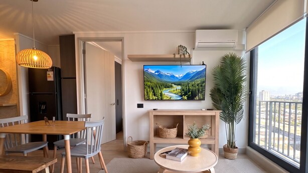 A modern living room with a large TV, dining area, and a view of the city. - Santiago Metro Ecuador - Domus Travels (Santiago)