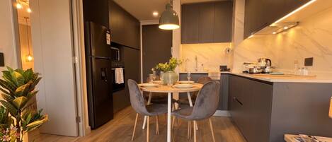 A modern kitchen with dark cabinetry, a central island, and a dining area with two chairs.