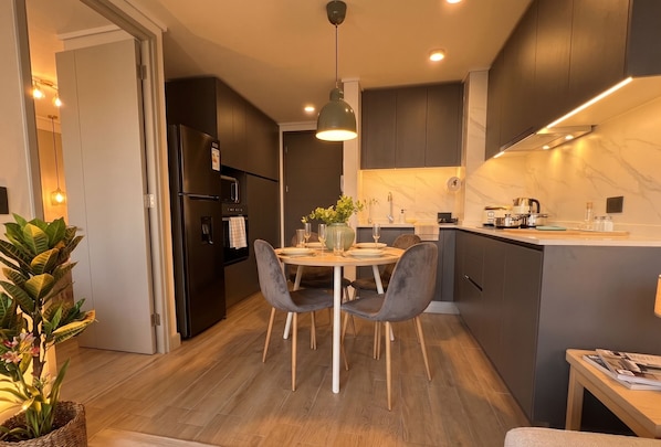 Una cocina moderna con armarios oscuros, una isla central y una zona de comedor con dos sillas.