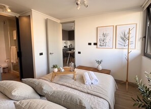 A modern bedroom with a bed, bedside tables, and a view into the kitchen. - Edificio O2 Santiago by Domus Travels (Santiago)
