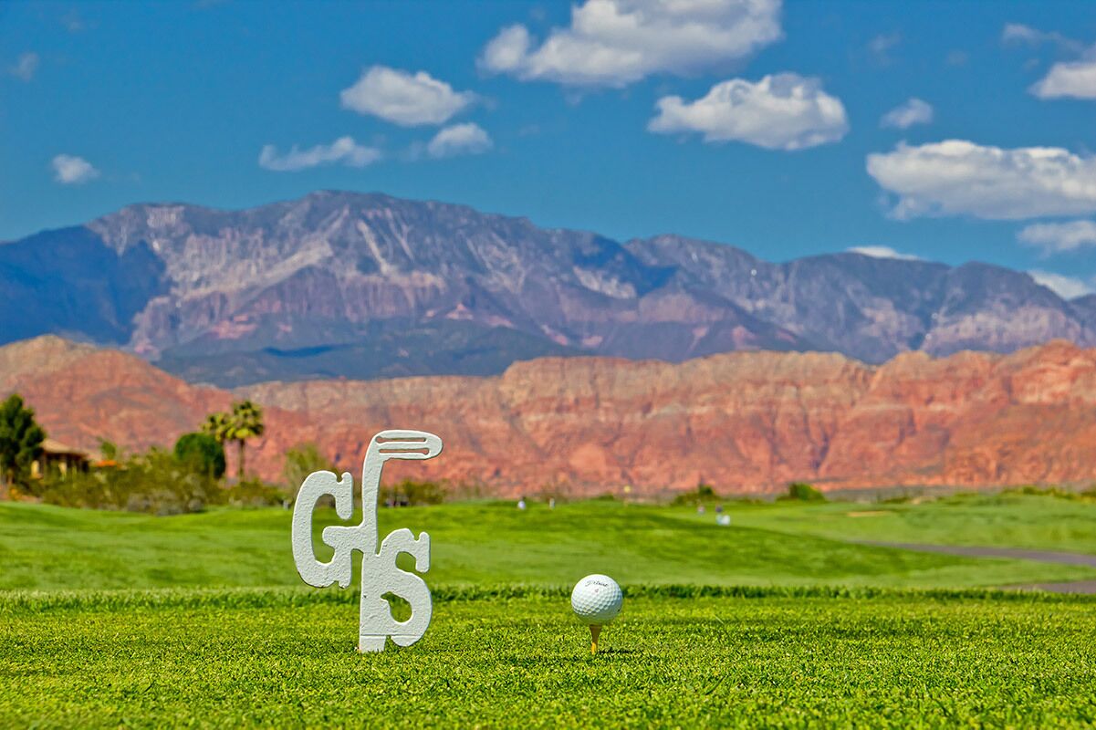 Campo de golf con un tee y pelota, montañas al fondo y cielos despejados.
