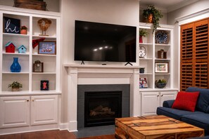 A living room with a fireplace, a television mounted above it, and a blue sofa with a red cushion. - 3 King Beds with En Suite Bathrooms and Private Shuttle to Square & Stadium (Oxford)