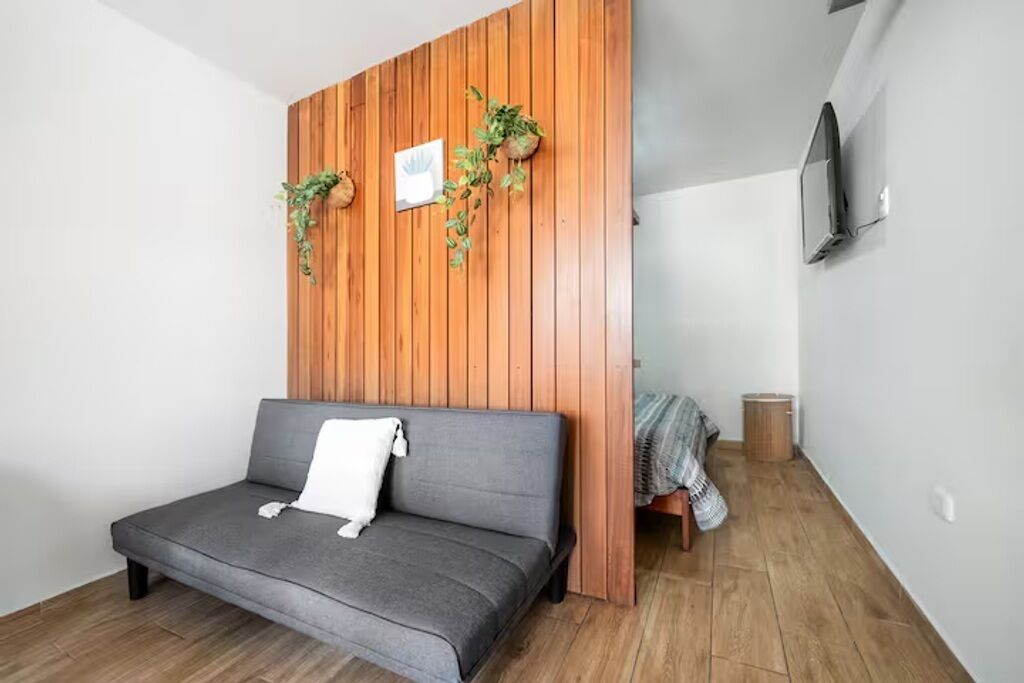Una habitación moderna con un sofá gris, panel de madera en la pared y un televisor montado.